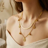 Layered gold necklace with flat herringbone chain and tree of life charms.