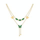 A layered emerald butterfly necklace and a golden bow-heart necklace on a black box.