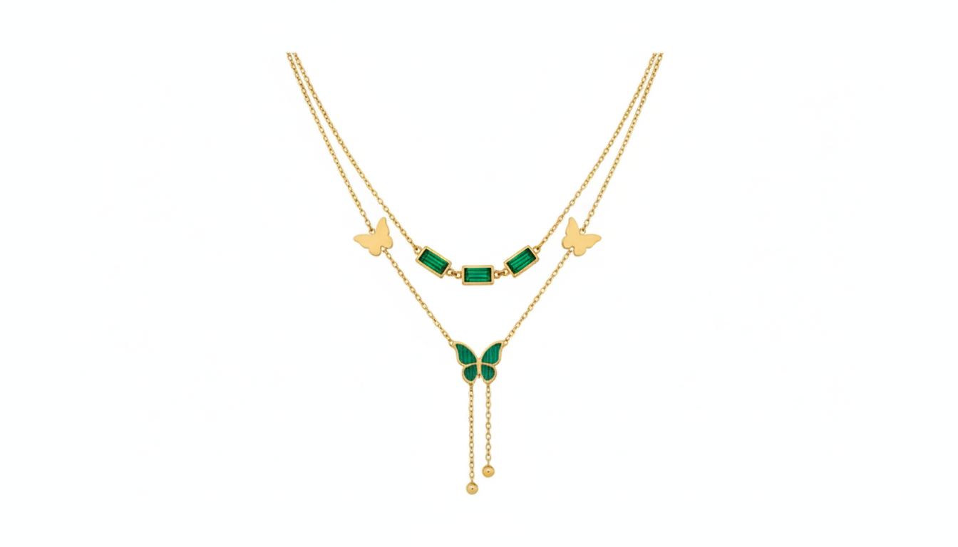 A layered emerald butterfly necklace and a golden bow-heart necklace on a black box.
