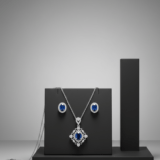 Blue sapphire pendant necklace and matching stud earrings on a black display stand.