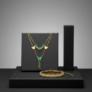 Layered gold butterfly necklace with green emerald accents and a diamond tennis bracelet on a black display.