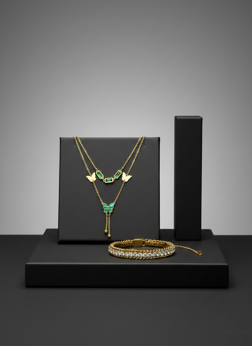 Gold Butterfly & Emerald Jewelry Set Layered gold butterfly necklace with green emerald accents and a diamond tennis bracelet on a black display.