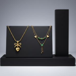 Gold heart bow pendant and emerald butterfly layered necklace on a black jewelry stand.