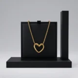 A gold-toned heart pendant necklace on a delicate snake chain against a clean, white background.